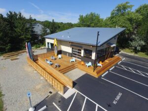 Liberty Remodeling & Construction modern commercial remodel featuring a sleek metal-roofed building with a large custom wood deck, surfboards, and outdoor seating.