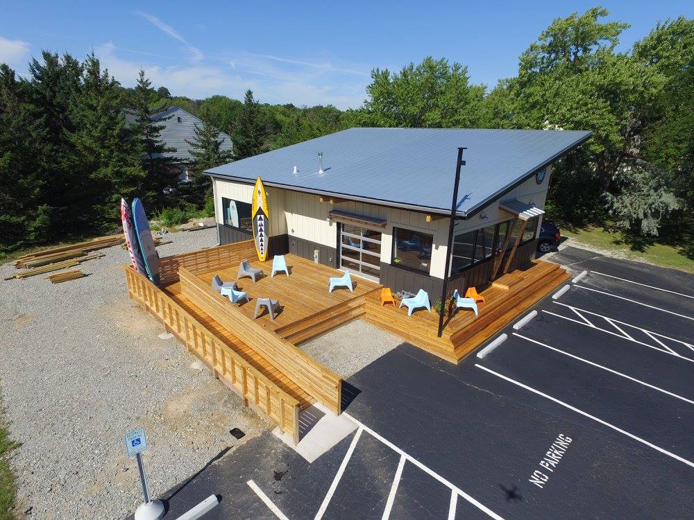 Liberty Remodeling & Construction modern commercial remodel featuring a sleek metal-roofed building with a large custom wood deck, surfboards, and outdoor seating.